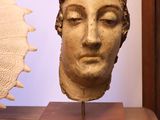 sculpture représentant une tête de femme, posée sur un socle en bois à côté d'un coquillage