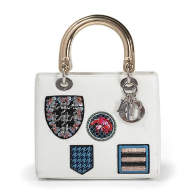 a white handbag with patches and a metal handle on a white background