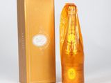 an orange bottle of perfume next to a gold box on a white surface