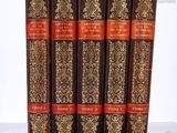 six vieux livres aux couvertures dorées et rouges posés sur une surface blanche
