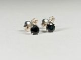 une paire de boucles d'oreilles à clous ornées de diamants noirs et blancs, posées sur une surface blanche