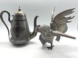 a silver teapot with a bird on it next to a silver teapot