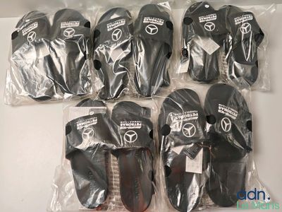 six paires de chaussons noirs et blancs dans des sacs en plastique, posées sur une surface blanche