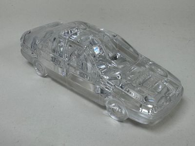 une petite voiture en plastique transparent posée sur une surface blanche