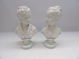 two white busturines of a woman and a man on pedestals