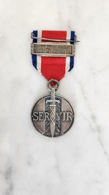 médaille d'argent ornée d'un ruban rouge, blanc et bleu posée sur une surface en marbre