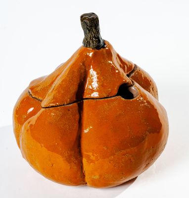 un petit objet en céramique en forme de citrouille posé sur une surface blanche