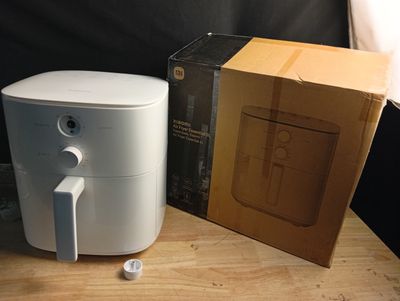 une friteuse à air chaud blanche posée sur une table à côté d'un carton