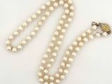 Gros plan sur un collier de perles blanches avec un fermoir en or