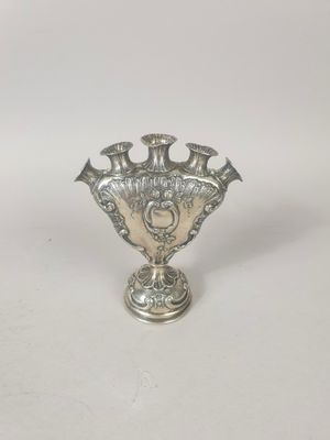 un vase ancien en argent posé sur une surface blanche, avec un fond blanc