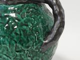 a green vase with a black handle on a white surface