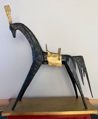 une sculpture de cheval en métal posée sur un socle en bois, elle-même posée sur une table