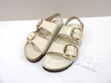 beige sandals with buckles on a white surface with a price tag
