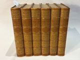 five antique books lined up in a row on a white surface