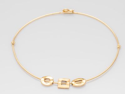 un collier ras-du-cou en or sur lequel est gravé le mot « she »