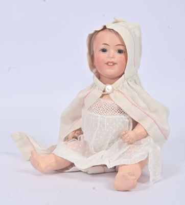 a doll that is sitting on the ground wearing a white dress and bonnet