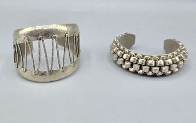 Deux bracelets manchettes en métal argenté. Le premier forma…