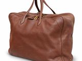 Le grand sac en cuir marron est posé sur une surface blanche.