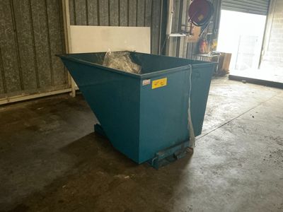 a blue dumpster sitting in a garage with a door open