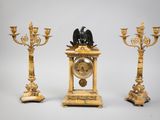 trois bougeoirs dorés et une horloge surmontée d'un oiseau
