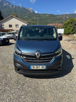 the front of a blue van parked in a parking lot with mountains in the background