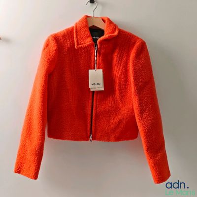 an orange jacket hanging on a hanger with a tag on it