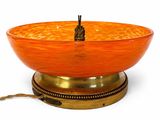 an orange glass bowl on a brass plate on a stand