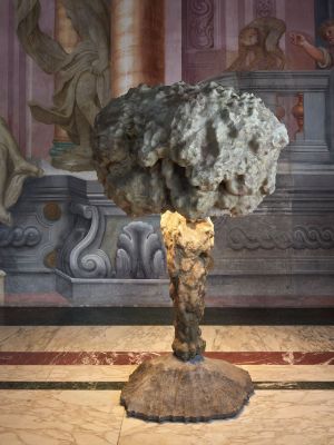 une sculpture représentant un arbre, posée sur un socle devant un mur