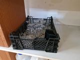 bottles and glasses in a plastic crate on a shelf in a kitchen