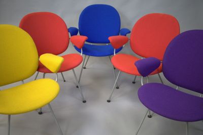 six chaises colorées disposées en cercle sur une surface blanche