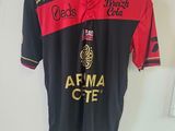 Le t-shirt est noir et rouge, et il y a une bouteille de bière imprimée dessus.