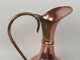 an old copper pitcher with a curved handle on a white surface