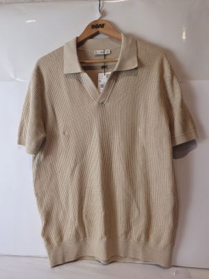 un pull beige suspendu à un cintre accroché au mur, devant un mur blanc