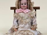 une poupée assise sur une chaise, avec un nœud rose