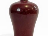 un vase rouge posé sur une surface blanche