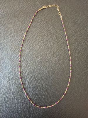 a necklace with pink and gold beads on a black leather surface
