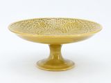 yellow glass bowl with decorative design on pedestal on white background