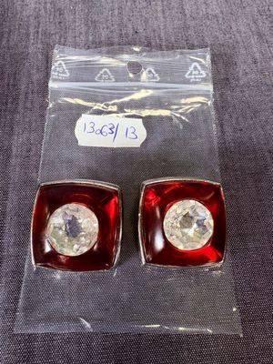 une paire de boucles d'oreilles à clous en cristal rouge et transparent, dans un emballage en plastique