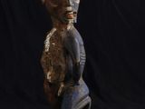 une vieille statue en bois représentant un homme assis sur un fond noir