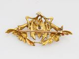 a close up of a gold brooch with leaves and flowers