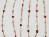 chaîne en or ornée de perles en cornaline et de perles de verre rouges sur fond blanc