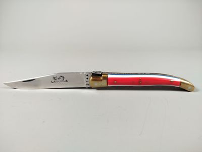 un couteau au manche rouge posé sur une surface blanche