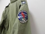 a green jacket with a patch on it hanging on a wall