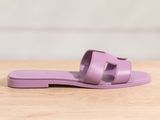 des sandales violettes posées sur une table en bois, avec un mur blanc en arrière-plan