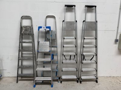Plusieurs échelles sont alignées contre un mur blanc dans un garage.
