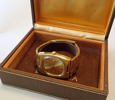 une montre en or dans un coffret marron posée sur une surface blanche