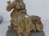 une statue représentant une femme assise sur un rocher à côté d'une cage à oiseaux