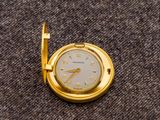 une petite montre de poche en or posée sur une surface marron