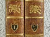 two old books are sitting on a table with a white background