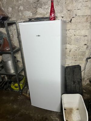 a white refrigerator in a dirty room with a red bottle on top of it